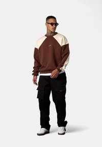 Brown and cream crew-neck sweatshirt with raglan sleeves, paired with black cargo pants. White sneakers complete the look.