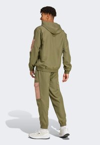 Olive green hooded jacket and matching joggers with pink accents and pocket details. Soft, smooth fabric; elastic cuffs and waistband.