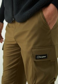Par nije brown cargo hlača s glatkom površinom, s bočnom džepu i crnim "berghaus" logotipom. Nosene s tamnim flis prslukom.