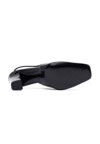 Zapato negro de charol con talón destalonado, con punta cuadrada y tacón cuadrado, visto desde la parte inferior sobre un fondo blanco.