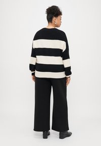 Svart og kremstripete genser med avslappet passform, lange ermer og ribbede mansjetter, kombinert med høyt liv sorte bukser og ankelstøvler.