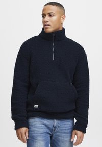 Marinefarget fleece-genser med høy krage, halv-zip-lukking, og frontlomme i kenguru-stil, med en strukturert overflate og elastiske mansjetter.