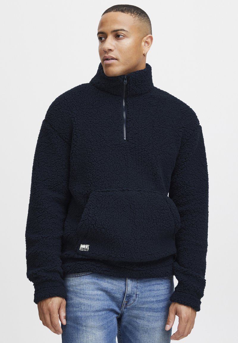 Marinefarget fleece-genser med høy krage, halv-zip-lukking, og frontlomme i kenguru-stil, med en strukturert overflate og elastiske mansjetter.