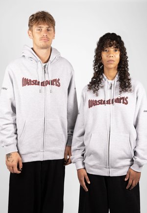 Sweatshirts à capuche zippés gris avec poches kangourou à l'avant. Présente un logo brodé "Waste Materials" en rouge foncé. Coupe ample avec cordons de serrage sur les capuches.