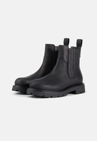 Botas de cuero negro hasta el tobillo con paneles laterales elásticos, suela de goma apilada y tiradores para facilitar su puesta. Textura suave, diseño duradero.