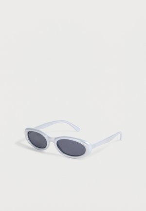 Lunettes de soleil ovales à monture blanche avec des verres teintés foncés reposant sur une surface blanche.