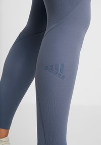 Legginsy wykonane z elastycznego, gładkiego materiału w stonowanym niebieskim kolorze, z delikatnie wytłoczonym logo na udzie oraz płaskimi szwami.