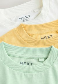 Trzy koszulki w kolorach białym, żółtym i miętowym ułożone jedna na drugiej. Każda ma prążkowany dekolt z widoczną metką "NEXT" z tyłu koszulki.