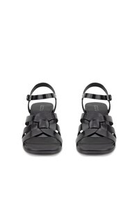 Juodos odinės sandalės su pintu dirželio dizainu, reguliuojama čiurnos saga ir plokščiu padu, pateiktos iš priekio ant balto fono.