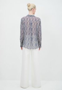 Camicia a maniche lunghe a quadri blu e bianca, realizzata in tessuto leggero. Presenta polsini con bottoni e colletto, indossata con pantaloni bianchi a gamba larga.