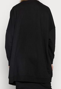 Person wearing an oversized black long-sleeve shirt viewed from behind against a plain light background.