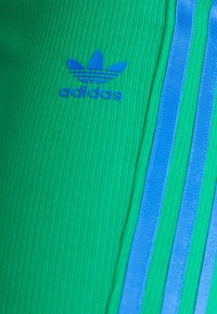 Grön ribbad träningsöverdel med blå tre-randig design och blå Adidas-logotyp på framsidan. Slät textur med en figurnära silhuett.