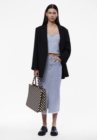 Fekete, oversized blézer, világoskék csíkos cropped top, hozzá illő, rojtos szegélyű szoknya, fekete slip-on cipők és kockás válltáska.