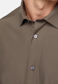 Camicia a maniche corte verde oliva con una texture liscia, colletto a punta e chiusura a bottoni. Presenta un dettaglio con bottoni in evidenza.