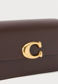 Brown leather wallet with a smooth texture; features a prominent gold "C" logo and contrasting stitching along the edges.