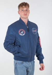 Granatowa kurtka bombowca z naszywkami NASA, prążkowanymi ściągaczami przy mankietach i u dołu. Posiada kieszenie boczne oraz zamek błyskawiczny z czerwoną zakładką na rękawie.
