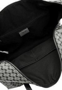 Intérieur d'un sac en tissu à motifs gris avec doublure noire, comportant une poche zippée et une étiquette de logo, soigneusement structuré avec une texture lisse.