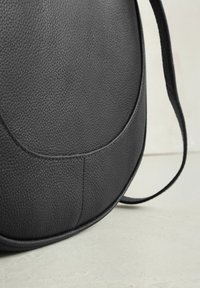 Černá kožená kabelka s texturovaným povrchem, zaobleným tvarem, prošitými detaily a nastavitelným popruhem. Hladký, odolný materiál.