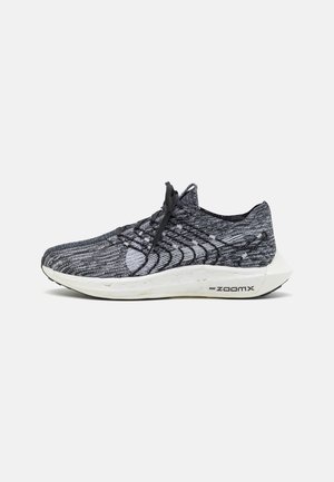 Schwarzer und grauer Strick-Laufschuh mit strukturiertem Obermaterial, runder Zehenpartie, elastischen Schnürsenkeln und weißer Zwischensohle mit "zoomx"-Markierung.