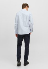 Cămașă în carouri de culoare albastră deschisă, cu guler structurat, mâneci lungi și manșete cu buton; asociată cu pantaloni închiși și pantofi casual negri.