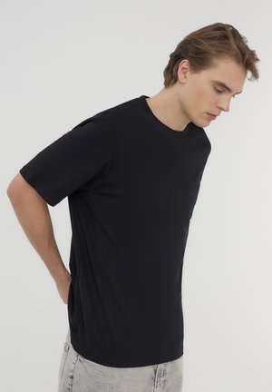 T-shirt in cotone nero con scollo rotondo e maniche corte, caratterizzato da una vestibilità rilassata e una superficie liscia, indossato con jeans chiari.