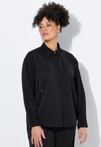 Camicia nera a maniche lunghe con pois bianchi, chiusura a bottoni e colletto classico, realizzata in un tessuto leggero e morbido.