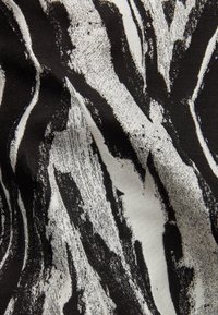Tissu noir et blanc avec des rayures abstraites ressemblant à des zèbres et des motifs texturés évoquant des coups de pinceau, montrant des plis et des creux dans le matériau.