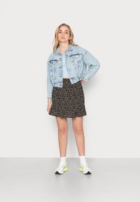 Casaco de ganga azul claro com dois bolsos frontais, combinado com uma saia preta com estampado floral. Modelo a usar ténis brancos com detalhes amarelos.