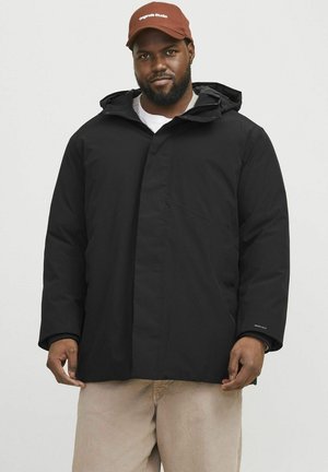 Black waterproof jacket with a hood, featuring a front placket closure, side pockets, and a tech label on the left sleeve. Casual fit design.