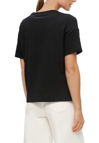 Zwarte katoenen T-shirt met korte, ribbelige mouwen en een relaxte fit, met een ronde hals en een rechte onderkant, gedragen met witte broek.