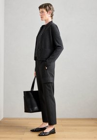 Cardigan en laine gris foncé avec des boutons, associé à un pantalon rayé foncé et des ballerines noires avec des accents en œillet. Sac tote noir à la main.