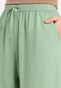 Lichtgroene loungebroek met een elastische tailleband, trekkoorddetail en zijzakken. Zacht materiaal met een licht gestructureerde afwerking.