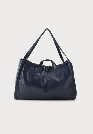 Bolso de hombro de cuero suave en color azul marino, con correas largas, un asa en la parte superior y un detalle anudado en el centro frontal, sobre un fondo claro y liso.