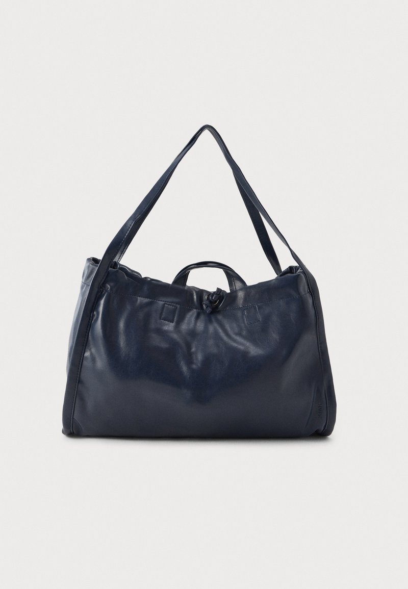 Pehmea tumesinine nahkne õlakott pika rihmaga, pealmise käepideme ja sõlme detailiga esiosas, mille taustal on ühtlane hele taust.