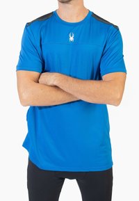 Camiseta deportiva de manga corta en azul brillante, con una textura suave, acentos negros en los hombros y un pequeño logotipo de araña blanca en el pecho.