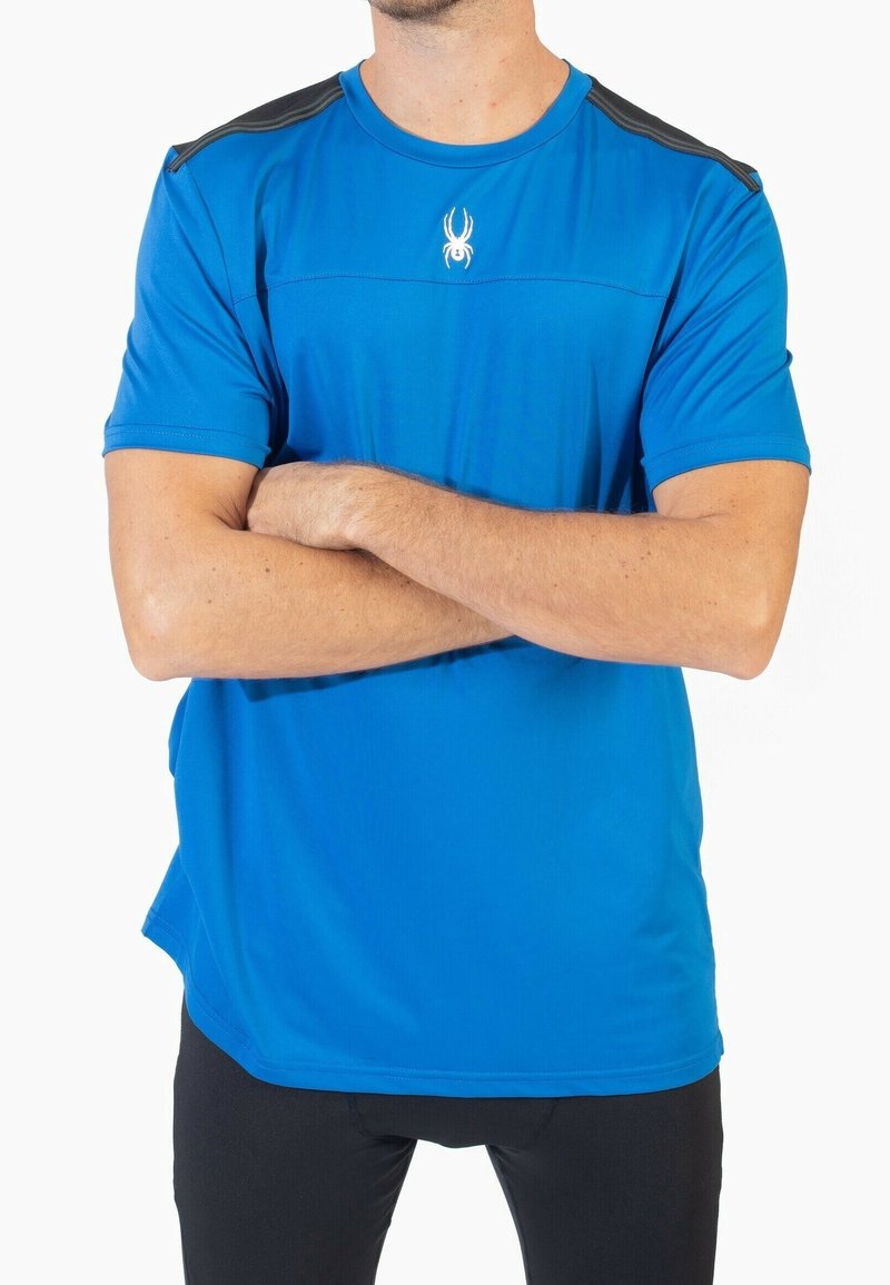 Camiseta deportiva de manga corta en azul brillante, con una textura suave, acentos negros en los hombros y un pequeño logotipo de araña blanca en el pecho.