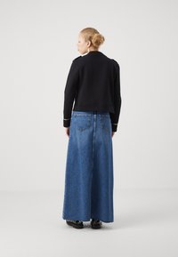 Veste noire cropped avec épaulettes, associée à une longue jupe en denim bleu, dotée de poches arrière et d'une silhouette droite.