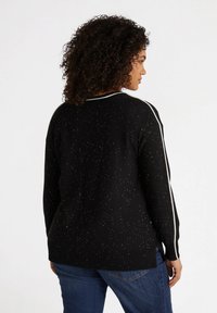 Pull noir avec une texture scintillante, rayures blanches le long des manches et ourlet côtelé. La vue de dos met en avant une coupe décontractée et les coutures des épaules.