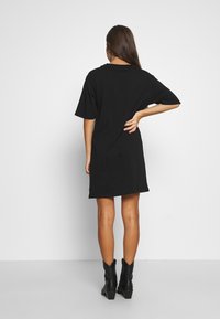 Musta lyhythihainen t-paitamekko, jossa on väljä istuvuus, pyöreä pääntie ja joka ulottuu puoleen reiteen, yhdistettynä mustiin nilkkabootseihin.