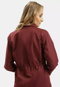 Bordowa kurtka z usztywnionym kołnierzem, regulowanym stanem i długimi rękawami. Gładki materiał z dopasowanym krojem, prezentujący minimalistyczny design.