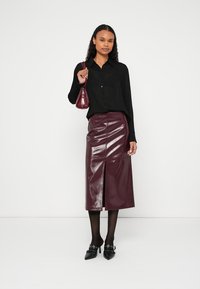 Μαύρο πουκάμισο με μακριά μανίκια και κουμπιά, σε συνδυασμό με φούστα μπορντό, γυαλιστερή, μήκους ως το γόνατο με σχίσιμο μπροστά, συμπληρωμένη με μαύρο καλσόν και παπούτσια.