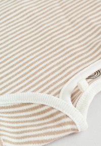 Un tissu à rayures beiges exhibe des lignes fines contrastées par du blanc. Une finition blanche arrondie complète le design du vêtement, avec un petit détail de bouton.