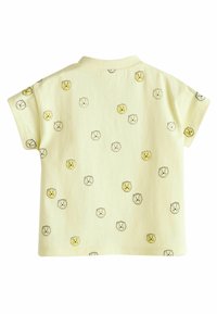 Gul tshirt med korte ærmer i en blød tekstur, der har et gentaget mønster af løvehoveder i sort og guld. Klassisk krave, løs pasform.
