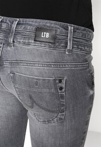 Jeans de mezclilla gris con un parche negro del logo de LTB en la parte posterior. Cuenta con dos bolsillos traseros con detalles de botones negros y sutilezas en las costuras.