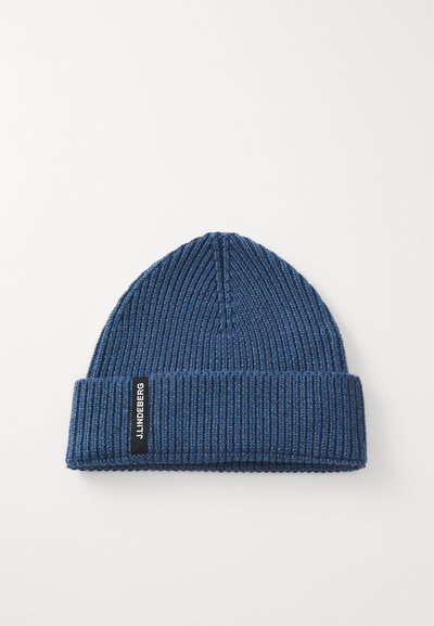 Navy blue knit beanie with a ribbed texture, featuring a fold-over cuff and a black logo tag on the side. Simple, snug design.