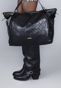 Grand sac à main en cuir noir avec un design matelassé et des détails en métal doré. Associé à des bottes en cuir noir montantes avec un accent de boucle.