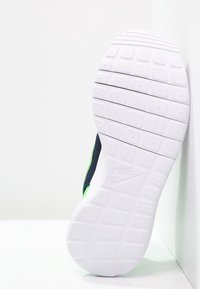 Bílá gumová podrážka s texturovaným vzorem a ohybovými drážkami. Tmavě modrá svrchní část se zelenými akcenty podél boků.