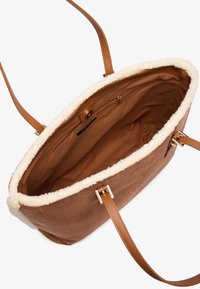 Sac fourre-tout en suède synthétique marron avec des détails en fausse fourrure crème, doté de deux poignées en cuir et d'une poche zippée intérieure pour un rangement en toute sécurité.