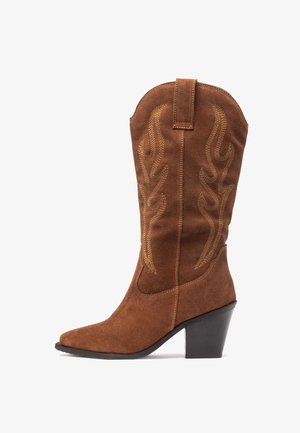 Botas de vaquero de ante marrón con punta afilada, que presentan costuras amarillas en patrones de llamas y un tacón negro apilado.