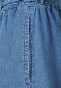 Blue denim fabric with an elastic waistband and a vertical slit pocket with visible stitching down the center.